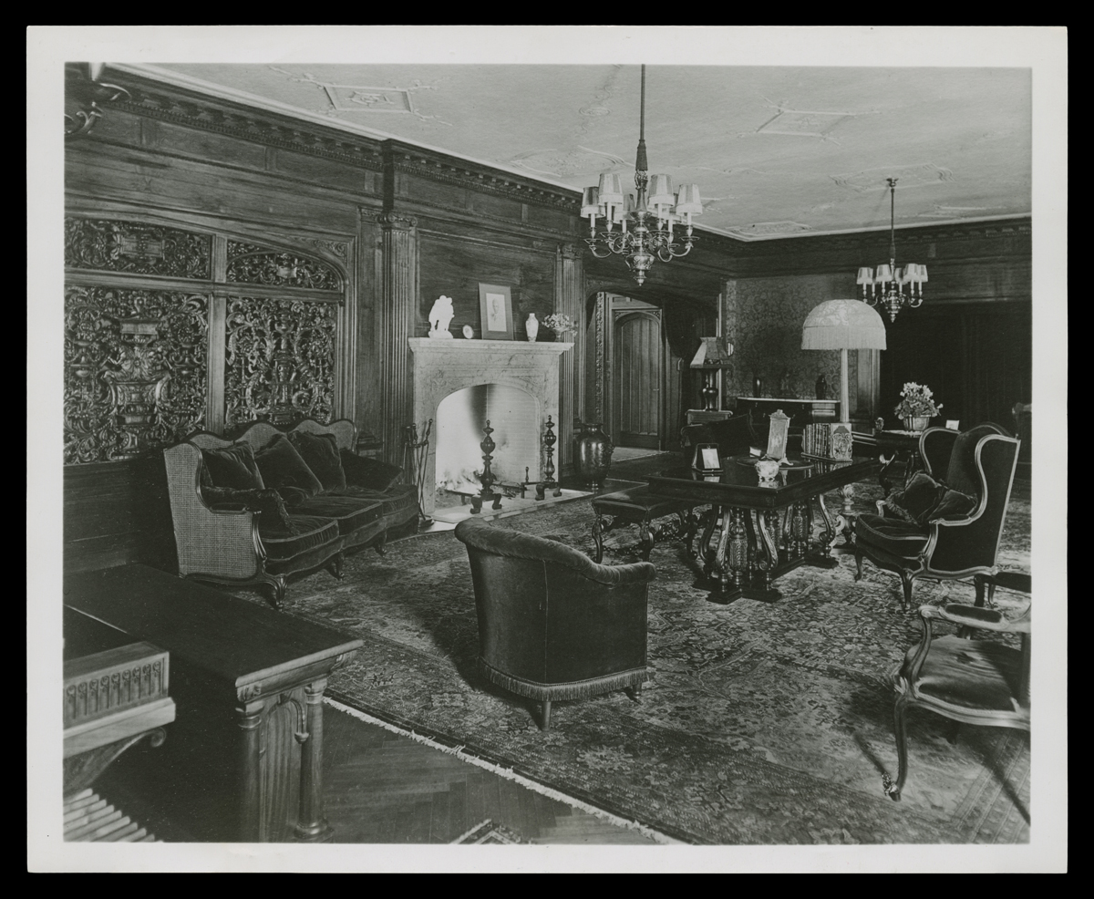 Room interior with intricately carved wood and fireplace, filled with upholstered chairs, a table, and other furniture