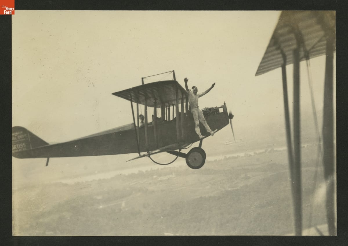 Man with arms upraised standing outside airplane in front of wing in midair