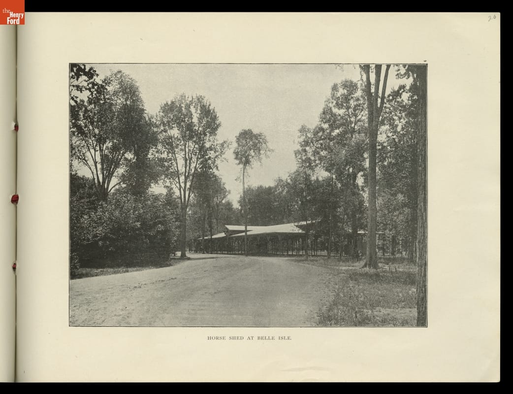 Black-and-white photo of large open shed by a road in a wooded area