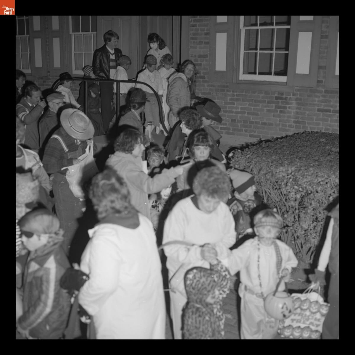 Crowd of adults and children, many in costume, outside brick house