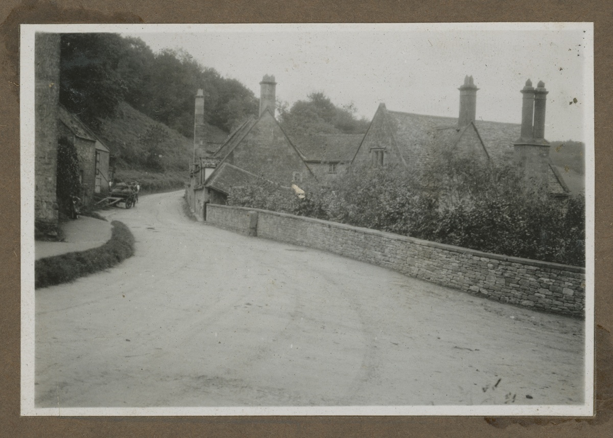 Photograph Album, Henry and Clara Ford's Visit to the Cotswolds, October 1930 / page 5 Curving dirt road with low stone buildings on either side and a wall on one side