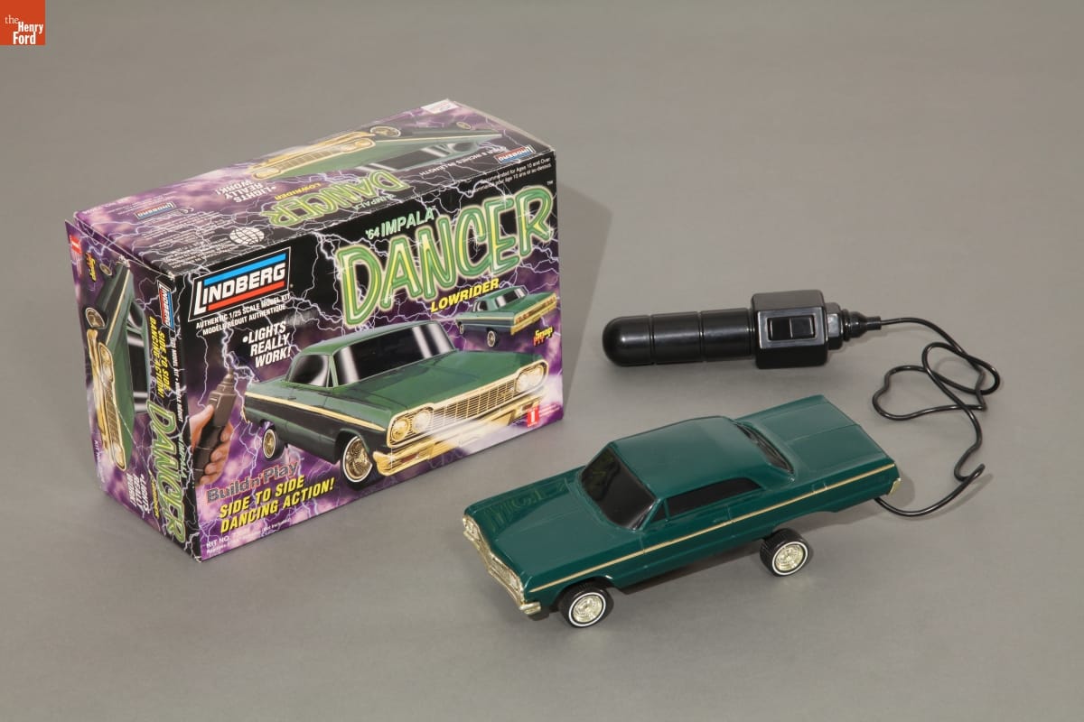 Dancin' 1964 Chevy Impala Model, circa 1999 Green toy car attached to black rod-like control, along with box with text, image of same car, and black and purple pattern of lightning bolts