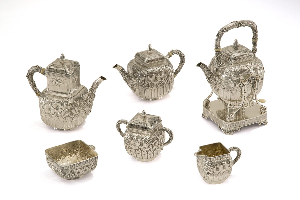 Silver pieces, including four pitchers of different shapes and sizes and two other containers, one with a lid, all elaborately decorated with bamboo, florals, and other decorative elements