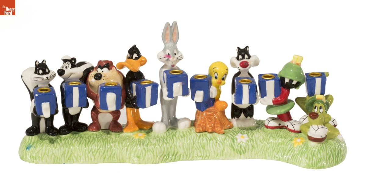 Nine sculpted cartoon characters, each holding a blue and white box with a hollow for a candle, on a base that looks like grass
