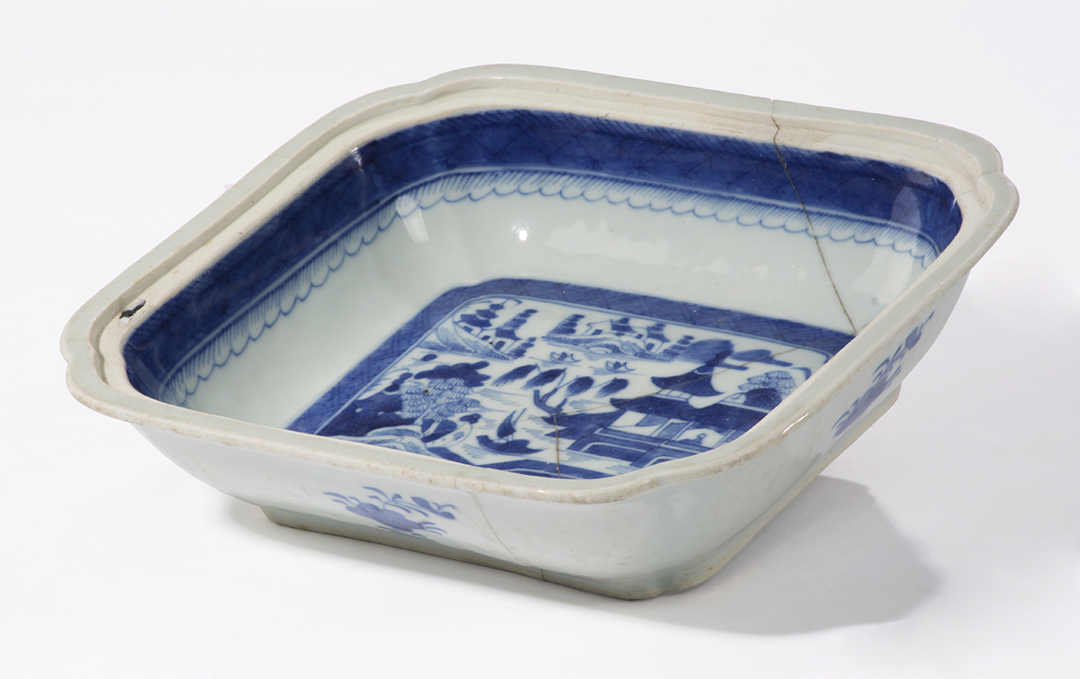 Side view of shallow, rectangular bowl with blue stripe around rim and image in blue of landscape with building