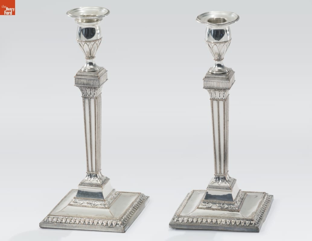 Silver candlesticks with wide square bases, pillar-like columns, and intricate decorative etching