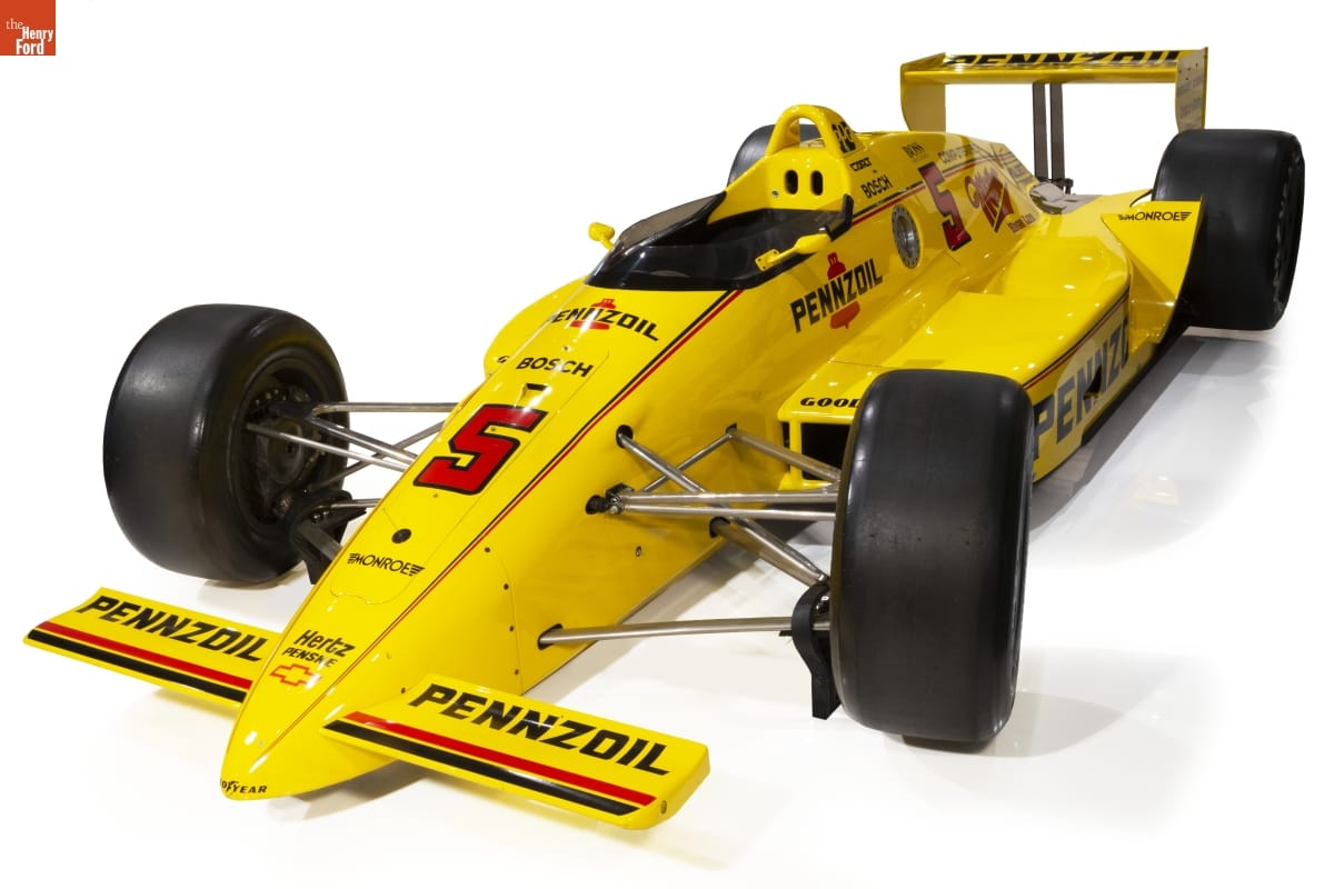 Low, bright yellow race car with large wideset tires and black and red text and decoration