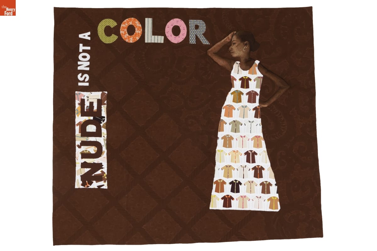 Brown quilt with text "NUDE IS NOT A COLOR" and quilted image of woman wearing dress with many short-sleeved shirts on it