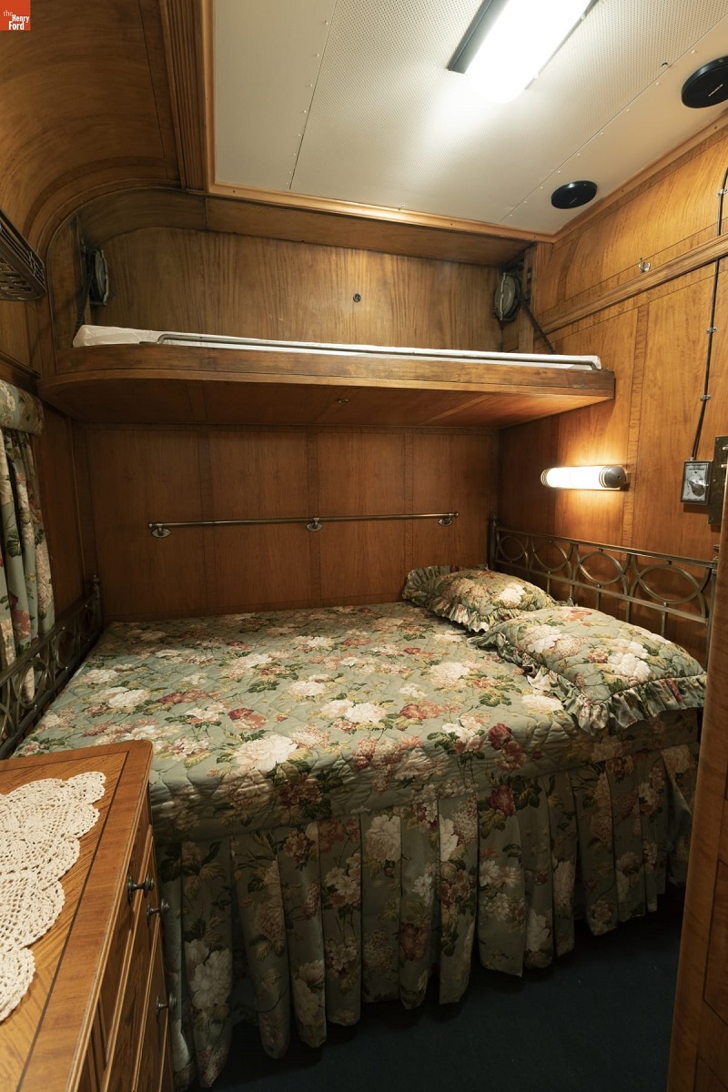 Room with wooden paneling, bed with shelf over it, and arched celing