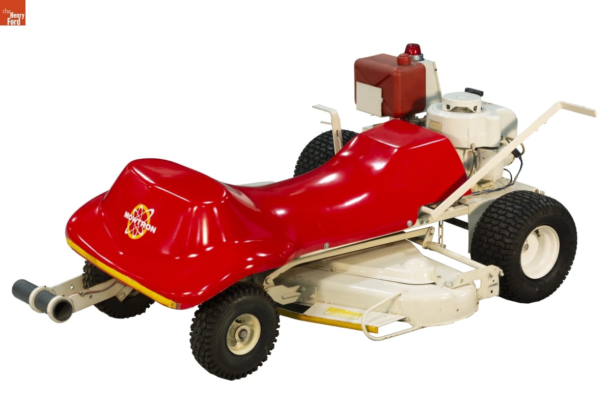 Low lawnmower with red plastic body on white platform with four black wheel