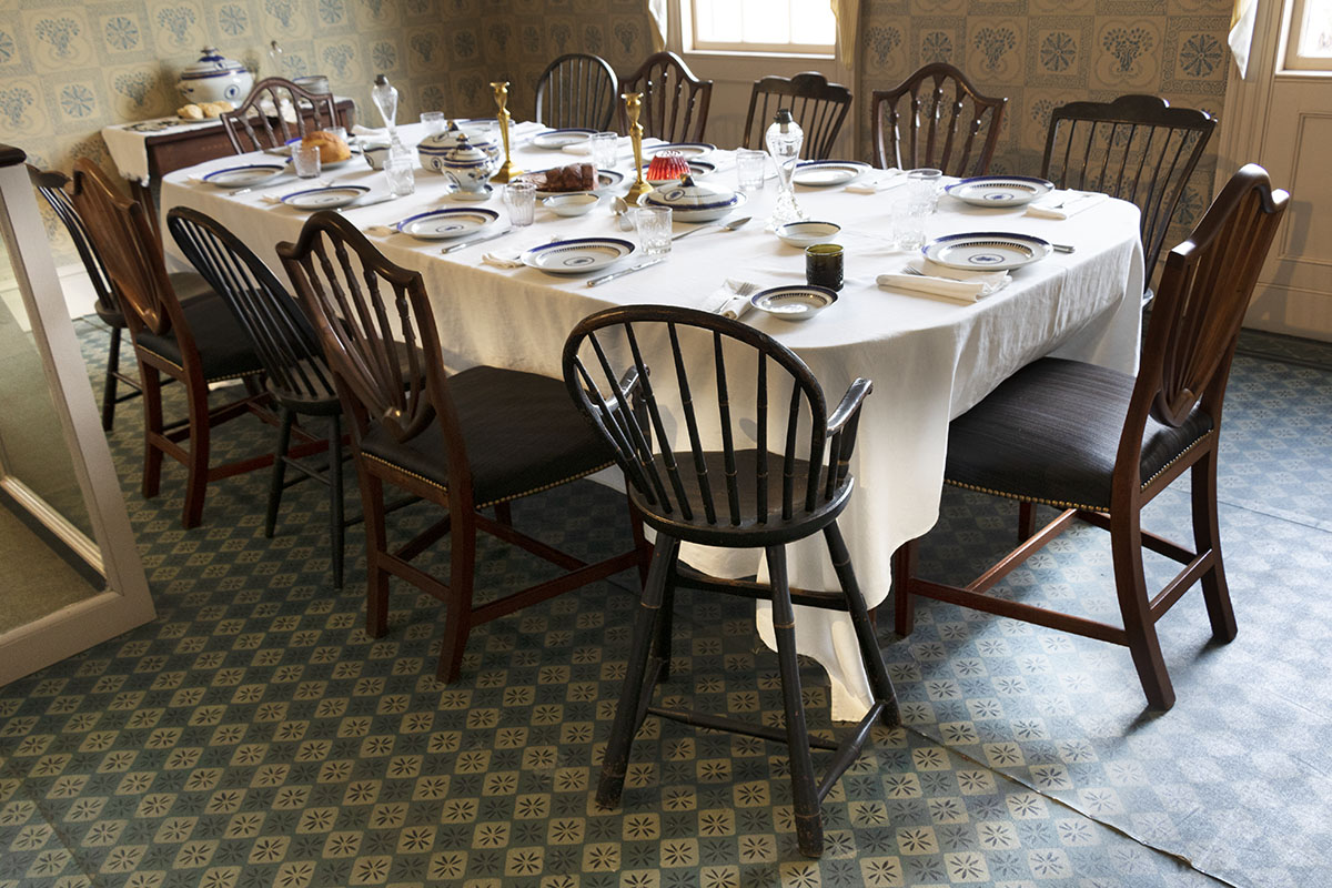 Noah Webster Home / dining room Room with patterned floor and walls containing a large, set table with many mismatched chairs