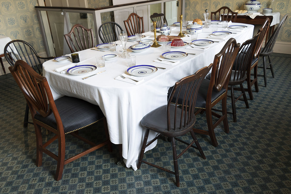 Noah Webster Home / dining room Long set table with mismatched chairs in room with patterned carpet and wallpaper