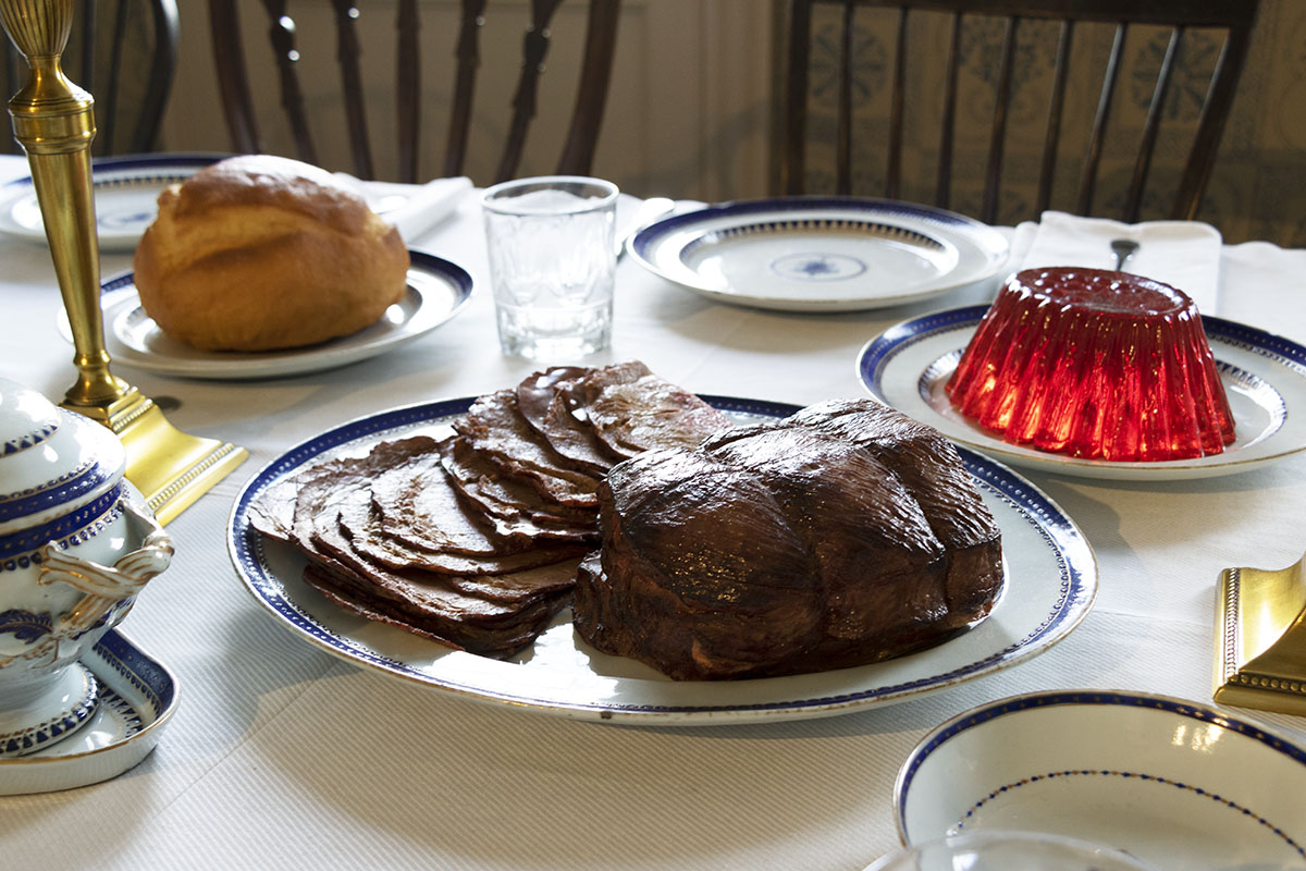 Noah Webster Home / table setting detail Meat roast (partially sliced), jello mold, and round loaf of bread on plates on table, with place settings nearby