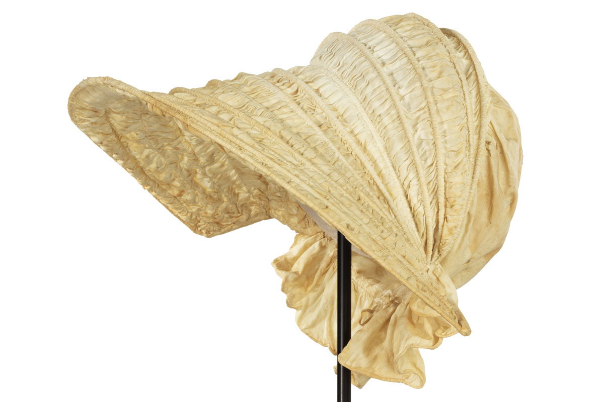 Off-white bonnet with rows of boning and shirred fabric between them; ruffle at neck