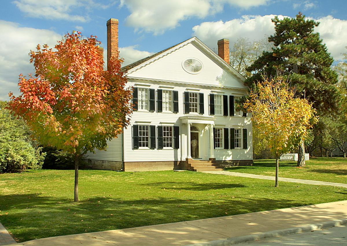 Two-story white house with black shutters, surrounded by lawn and a few trees