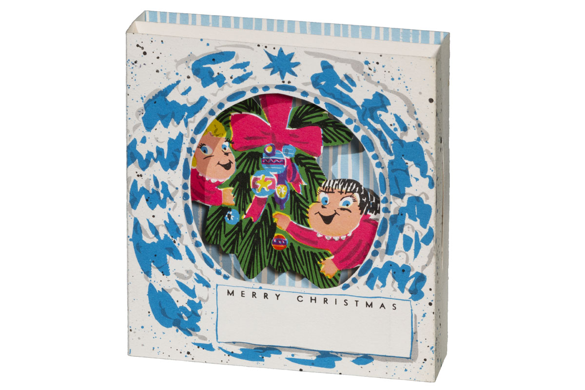 Three-dimensional blue and white paper card with cut-out circle in middle revealing two children, Christmas ornaments, and holiday greenery 