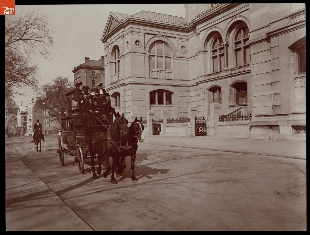 Horse-Drawn Omnibus on Fifth Avenue, New York City, 1900-1906 Two horses pull a large carriage loaded with people along a street lined with large buildings