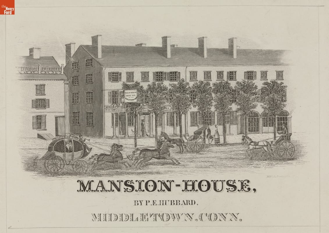 Horses and carriages passing on a road in front of a long, three-story building with a row of trees in front; also contains text