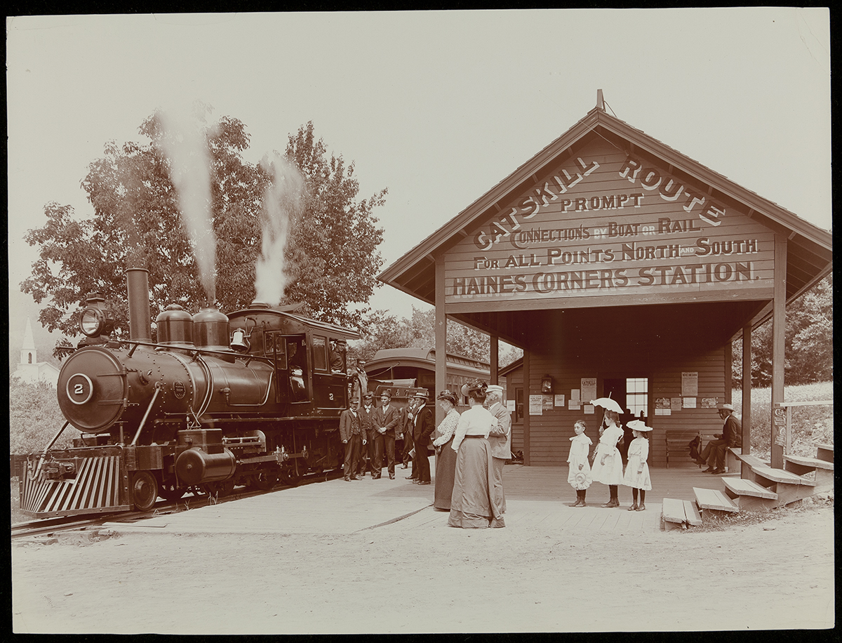 Photo of train with steam coming from it at tentpole-like station with a number of people standing around