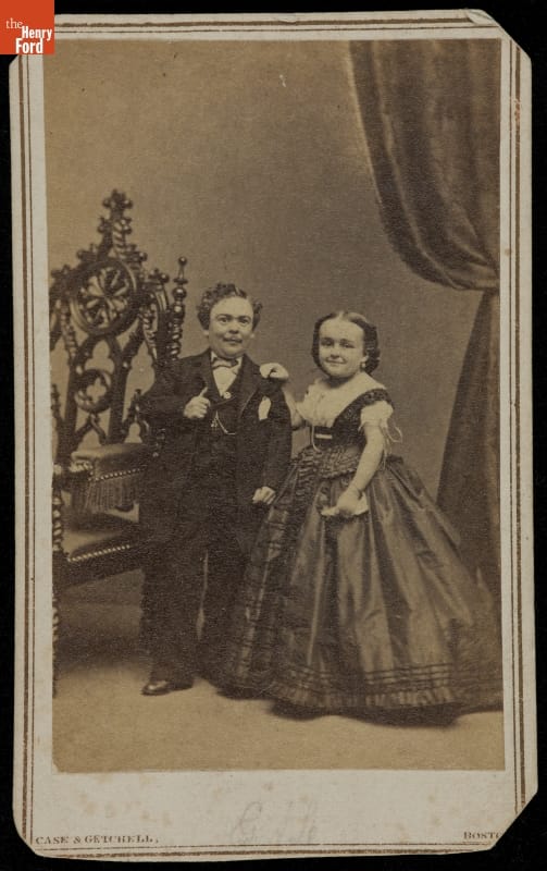 General Tom Thumb and Lavinia Warren, 1863-1870 Man and woman in formal suit and dress stand beside large chair