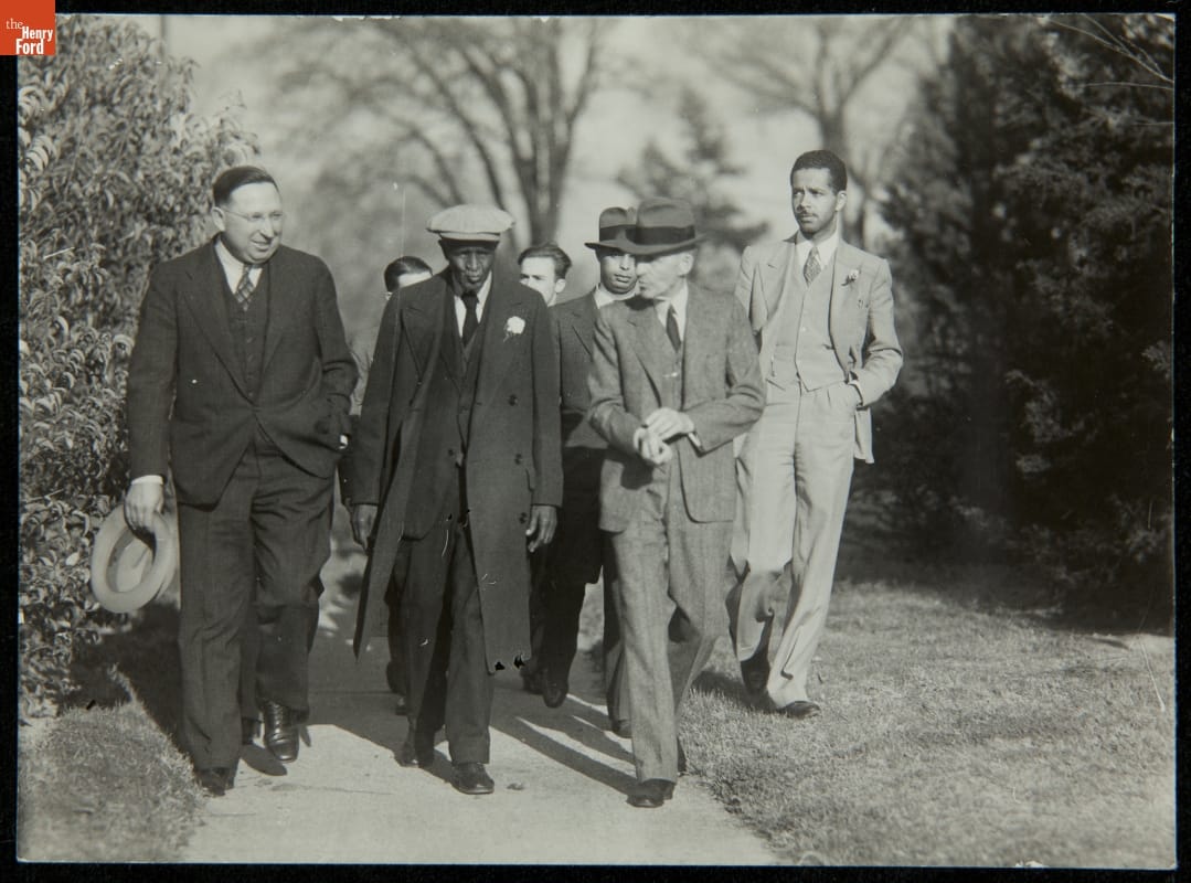 George Washington Carver and Henry Ford on the Tuskegee Institute Campus, 1938 Group of men walk on a sidewalk between grass and trees