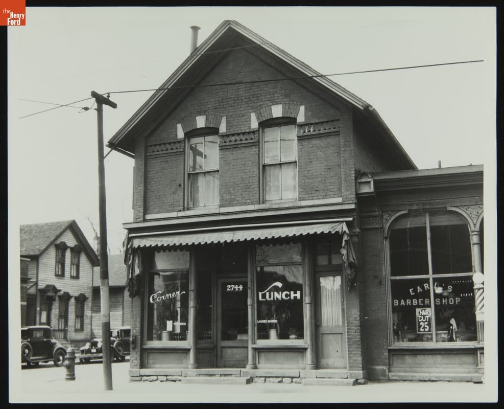 Exterior of Mrs. Cohen's Millinery Shop at its Original Site, Detroit, Michigan, 1935 Black-and-white photo of street scene, focused on two-story brick building with business windows on first floor