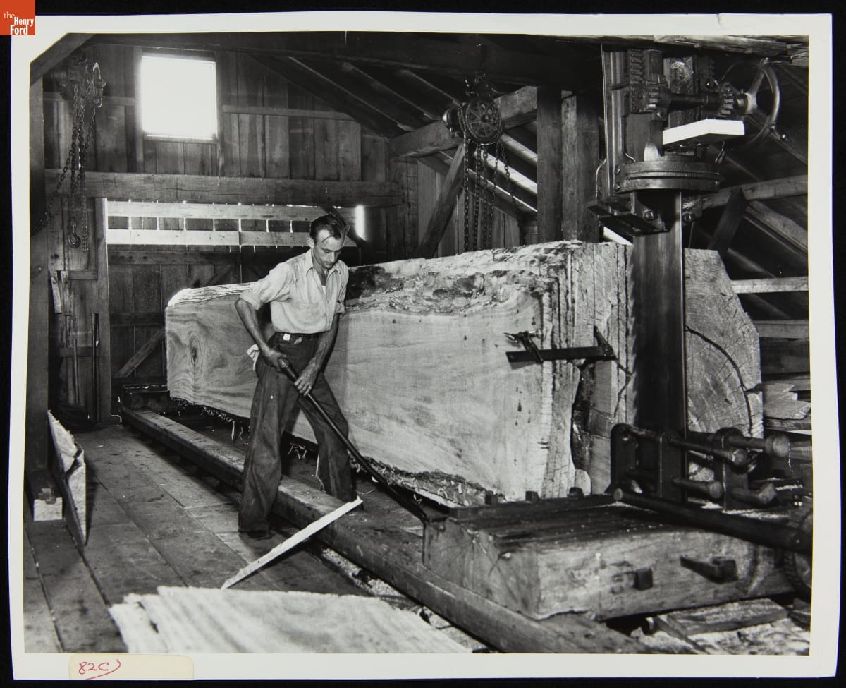 A Man Working in the Tripp Sawmill in Greenfield Village, June 15, 1936 Black-and-white photo of man working next to very large tree trunk mounted on a machine in a wooden building
