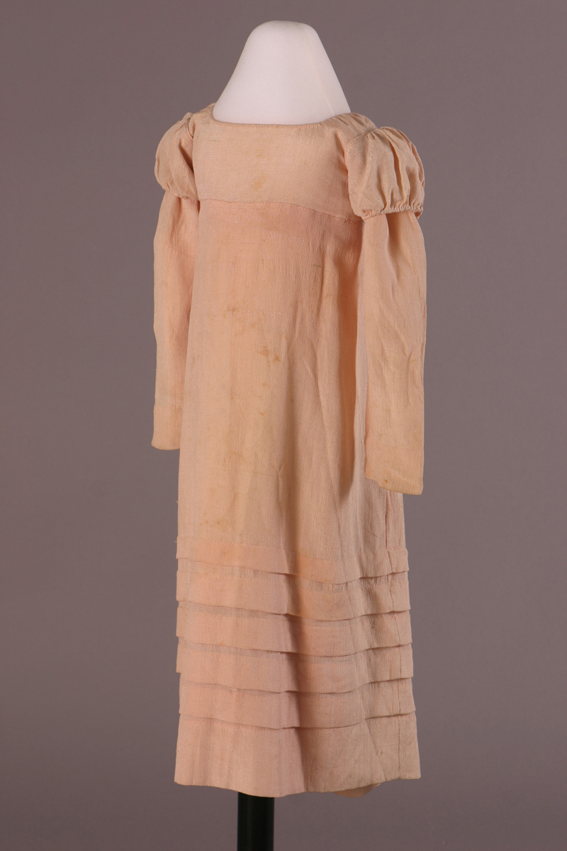 Pale pink dress with empire waist; slight puff at top of long sleeves; tiers at bottom of body