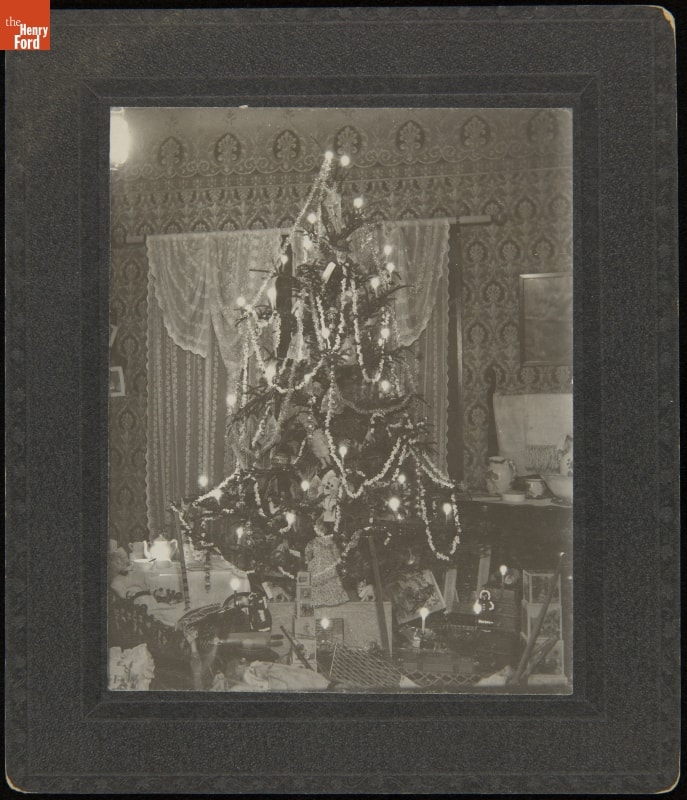 Matted black-and-white photo of a Christmas tree covered in decorations and surrounded by packages
