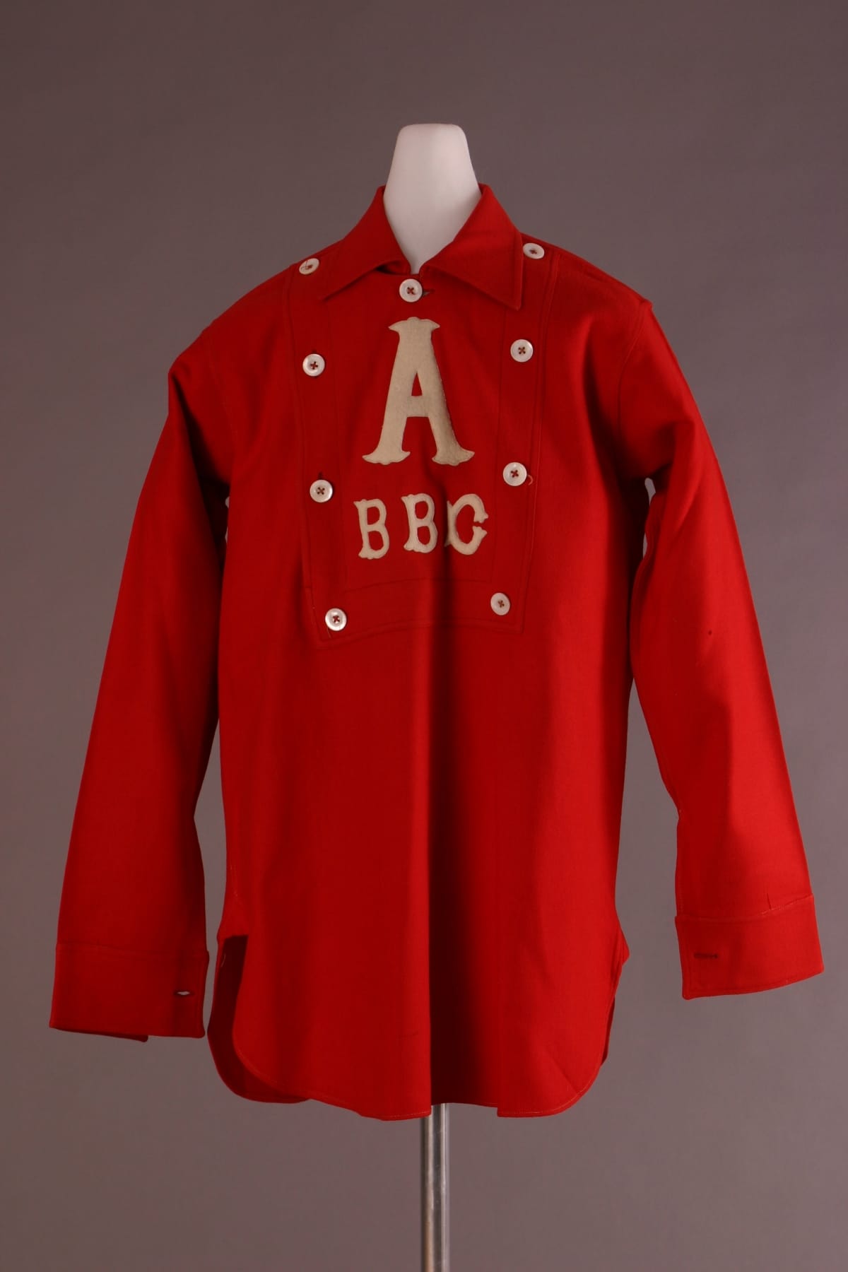Red shirt with collar and white buttons around the placket, featuring white letter "A" followed by "BBC"