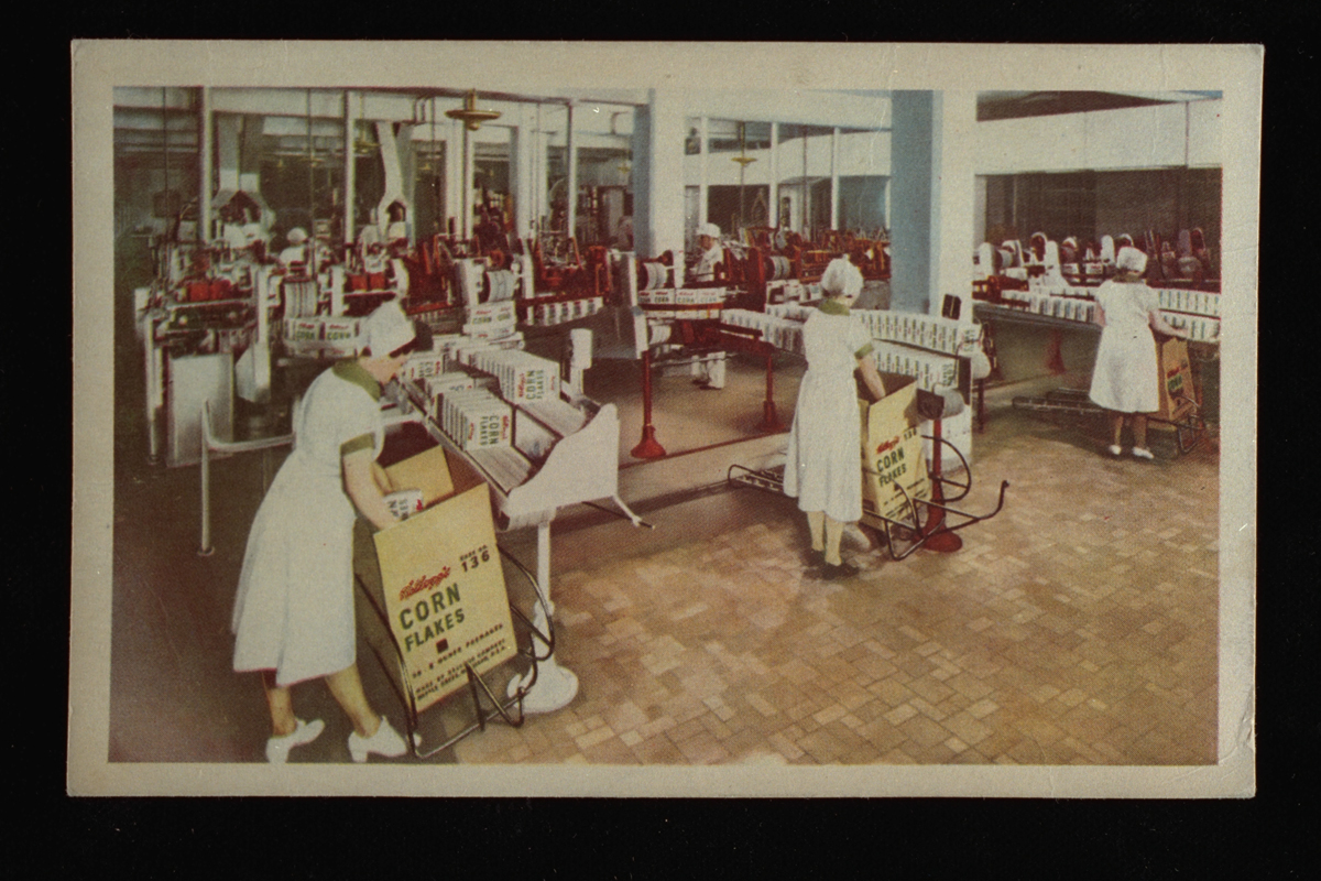 Postcard of Kellogg’s corn flakes packing room, c. 1935, with women in white dresses and hair coverings packing corn flakes boxes into large cartons