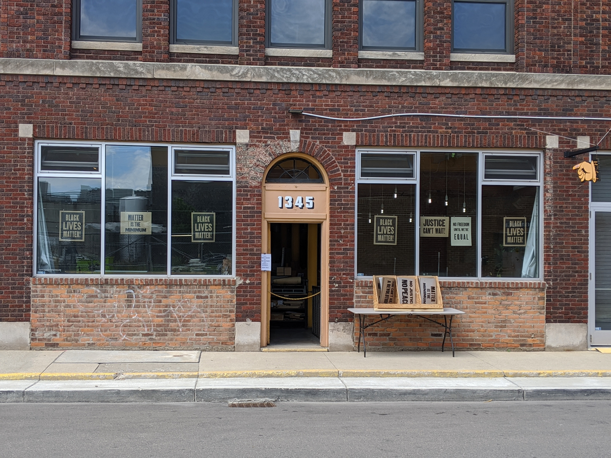 Storefront in brick building with posters hanging in windows and a table with bins of posters in front