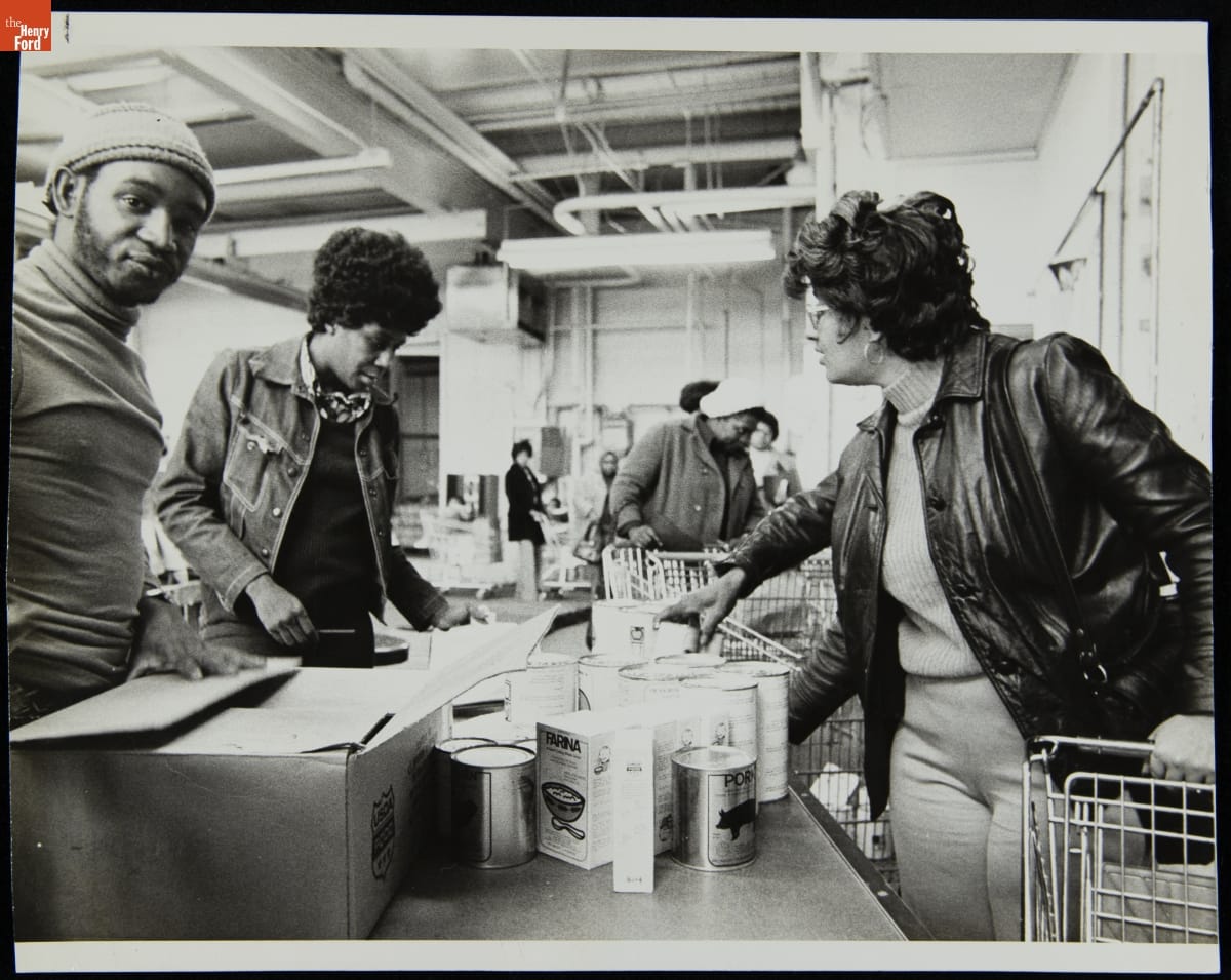 Depression's Harsh Impact at the Focus: HOPE Food Prescription Center in Detroit, March 1975 People of color stand by tables containing food in an industrial-looking space