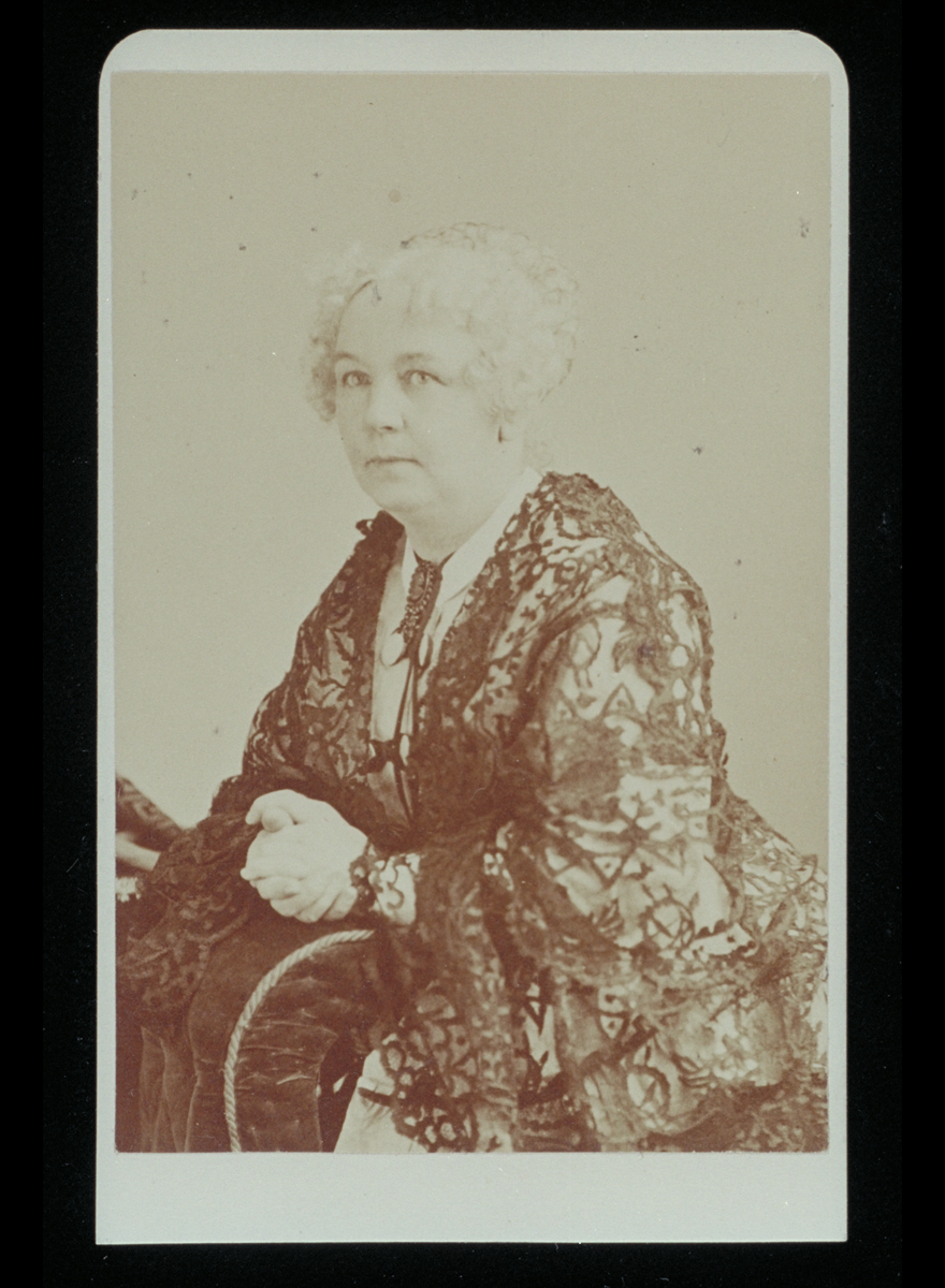 Portrait of Elizabeth Cady Stanton, circa 1870 Black-and-white portrait of woman with light-colored hair and clasped hands wearing elaborate lace dress.