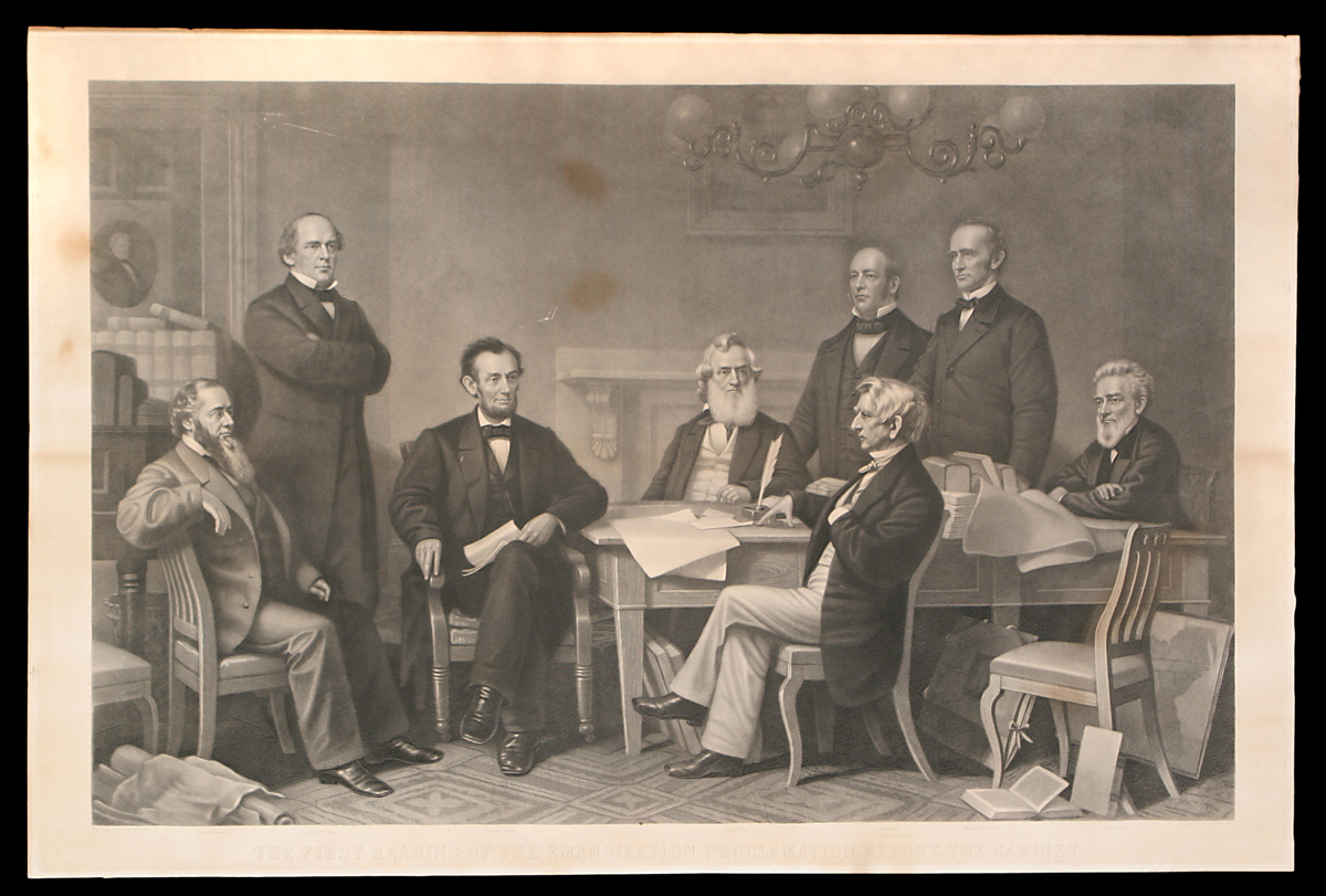 Group of men sit and stand around a table filled with papers and books, with additional papers and books around the room