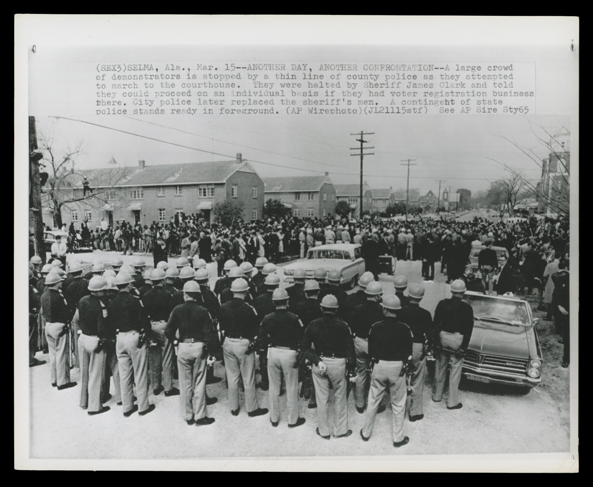 THF730281 Police block a street in Selma, Alabama, on March 15, 1965, as voting rights demonstrators attempt to march to the Dallas County Courthouse. Brown Chapel AME Church is visible in the background.