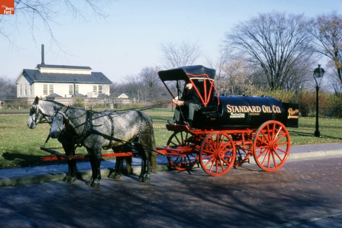 Two dappled horses hitched to a wagon with a black tank containing text for a body and four red wheels