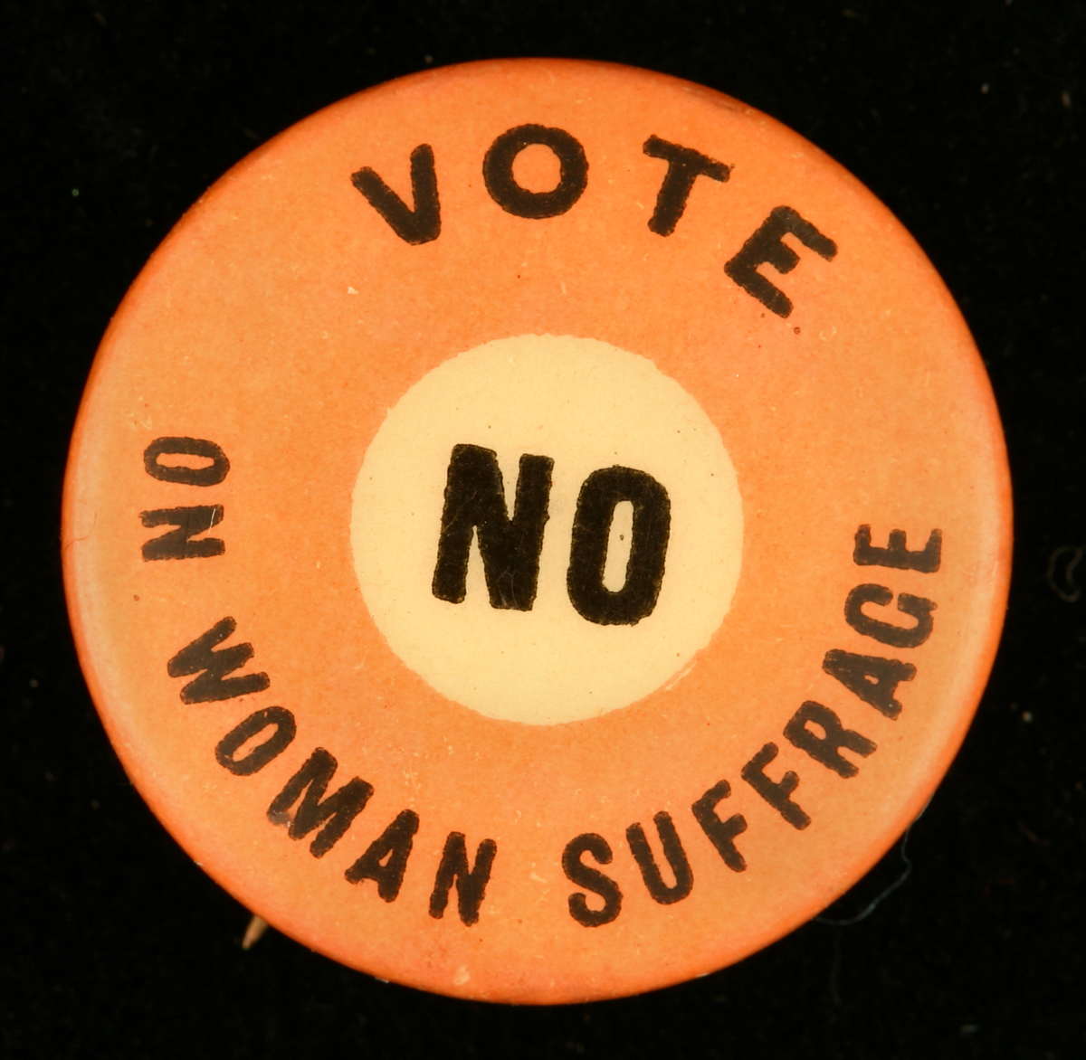 Button, "Vote No on Woman Suffrage," circa 1910 Round orange button with yellow circle in center, with printed text reading “Vote no on woman suffrage”
