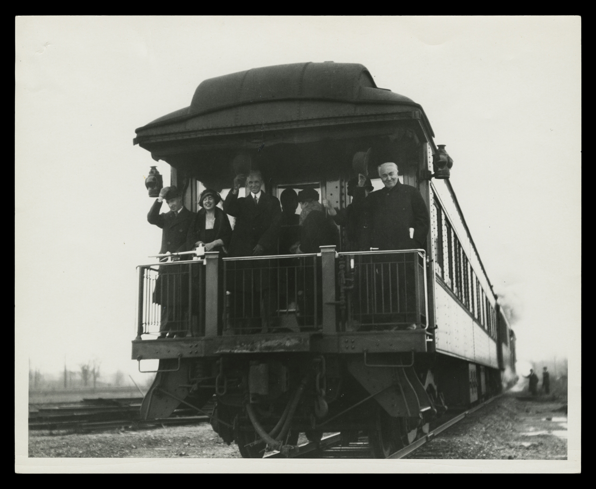 Edsel and Eleanor Ford, Henry and Clara Ford, and Mina and Thomas Edison on the Private Railroad Car "Fair Lane," circa 1923 Black-and-white photo of six people on the back platform of a rail car, most of them smiling and waving