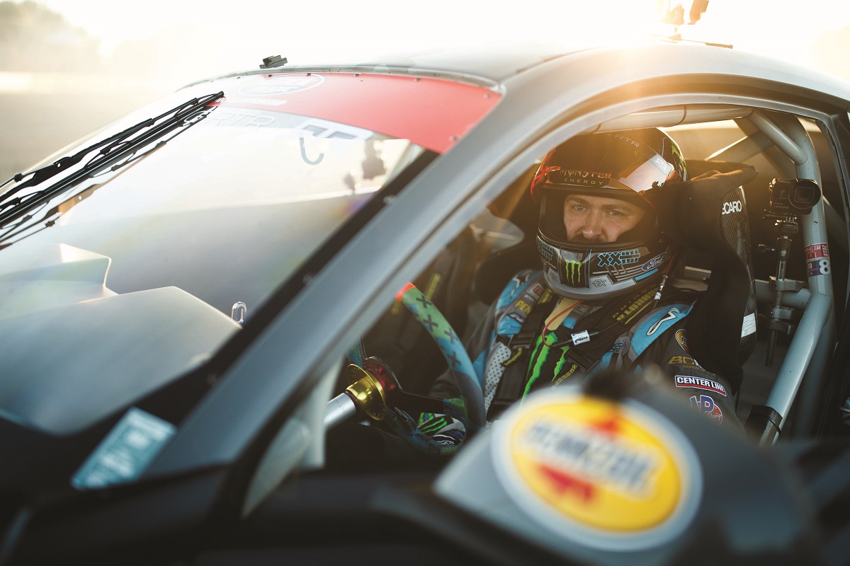 Vaughn Gittin, Jr. Tight shot of a man in racing helmet and jumpsuit sitting in race car sunlit from behind