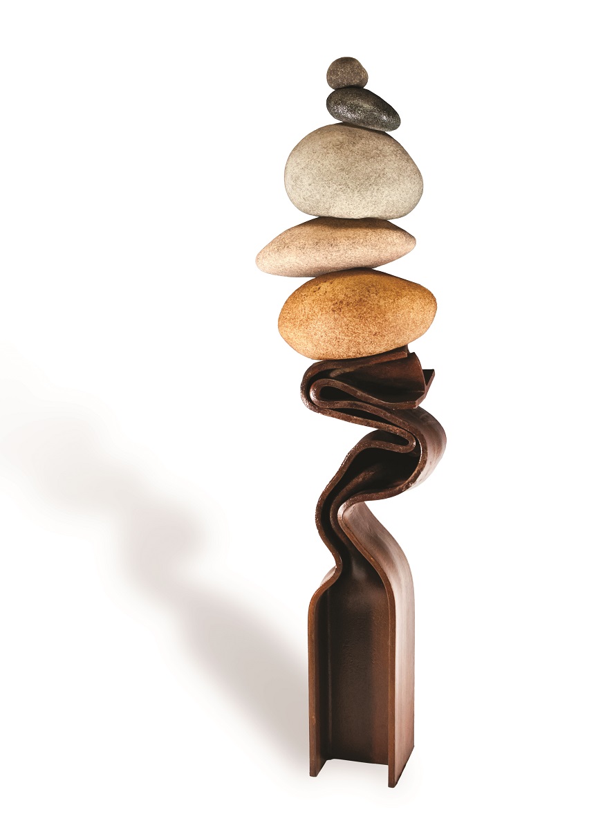 Five variously colored rounded rocks balance on top of each other atop what seems to be a melted and serpentine metal beam