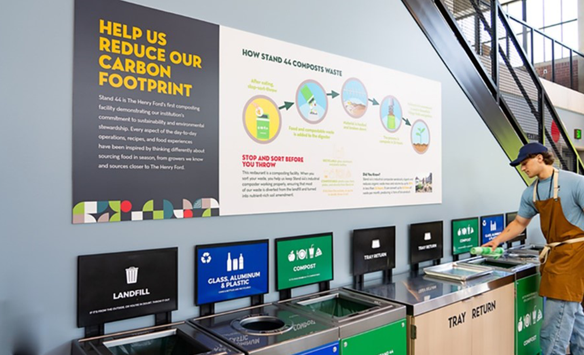 several garbage, compost, and recycling bins and a man in an apron cleaning a tray nearby